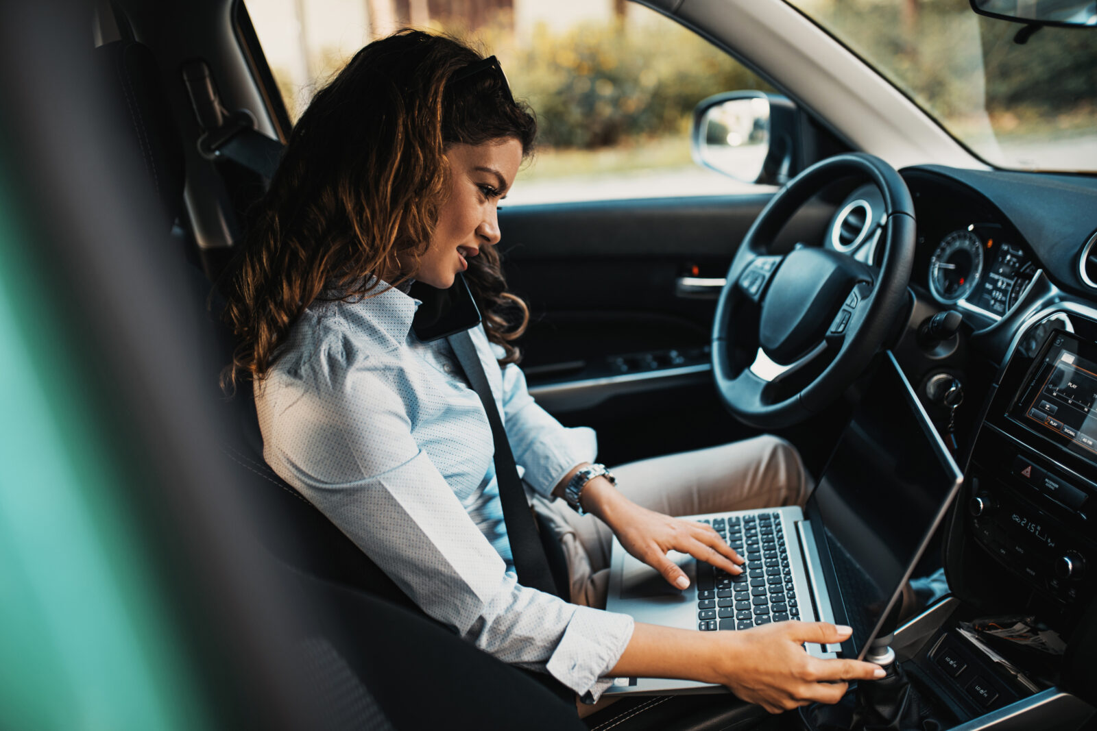 Beautiful young businesswoman driving car and using laptop.